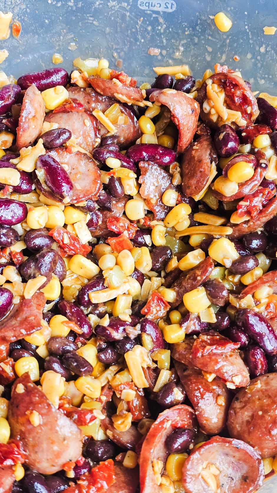 Close up of BBQ smoked sausage dense bean salad with black beans, dark red kidney beans, corn, crispy sausage slices, sun dried tomatoes, banana peppers, and shredded cheddar
