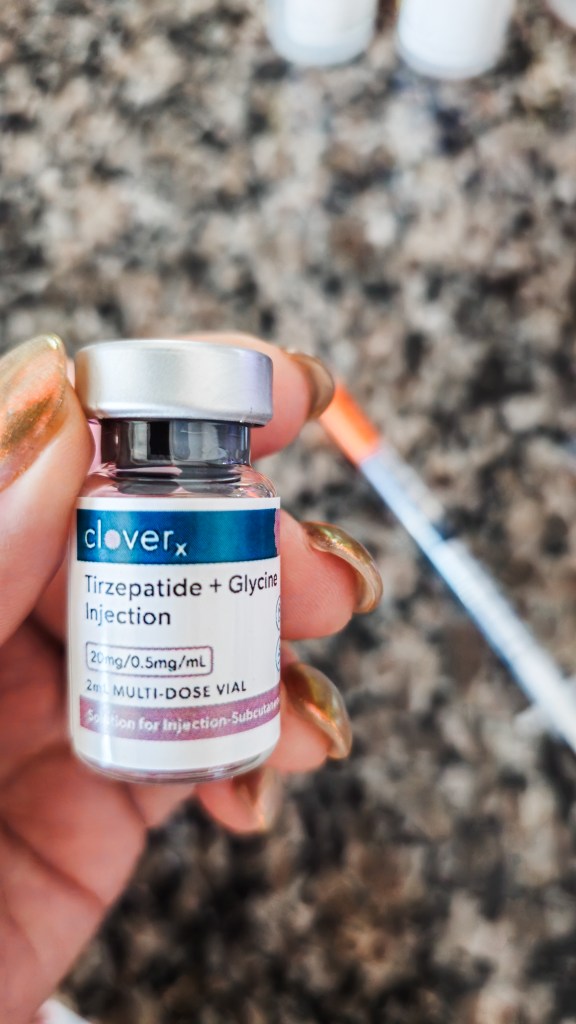Hand holding a CloverRx compounding pharmacy tirzepatide plus glycine injection vial at 20mg/0.5mg/mL with a syringe visible in the background — EllieMD's dedicated compounding pharmacy