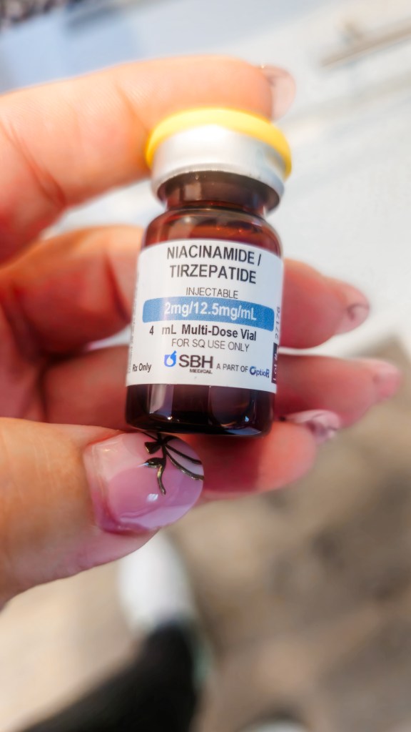 Hand holding an SBH Medical niacinamide tirzepatide injectable vial at 2mg/12.5mg/mL showing a different compounding pharmacy concentration than other providers