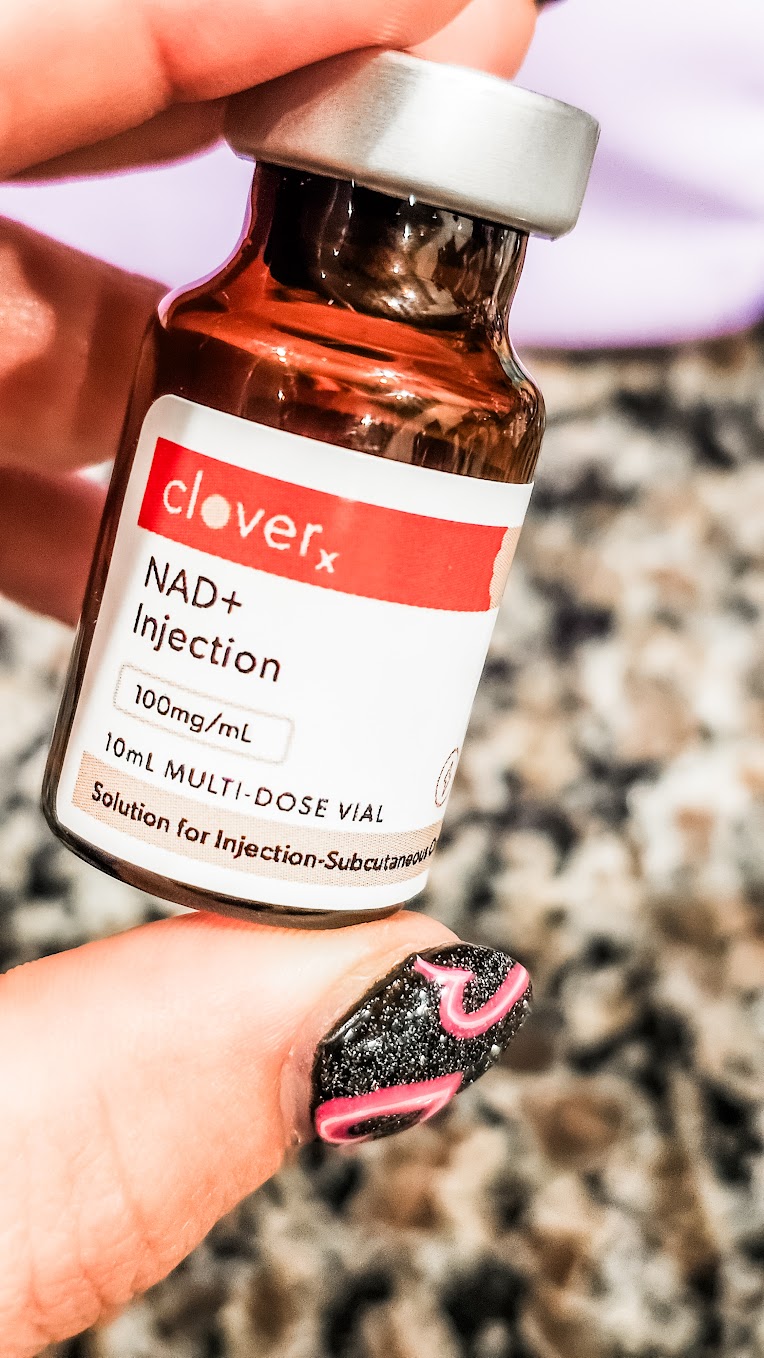 Close-up of a CloveRX NAD+ injection vial prescribed through EllieMD telehealth, 100mg/mL subcutaneous solution, held against a blurred granite background